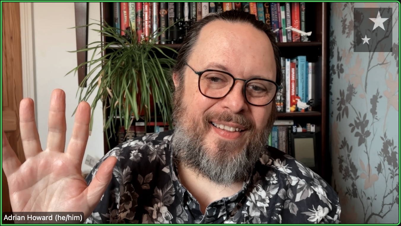 Screen shot of Adrian Howard on a Zoom call. He's a white male with a beard, dark hair going to grey, wearing reading glasses. His wearing a black shirt covered in white/grey flowers.