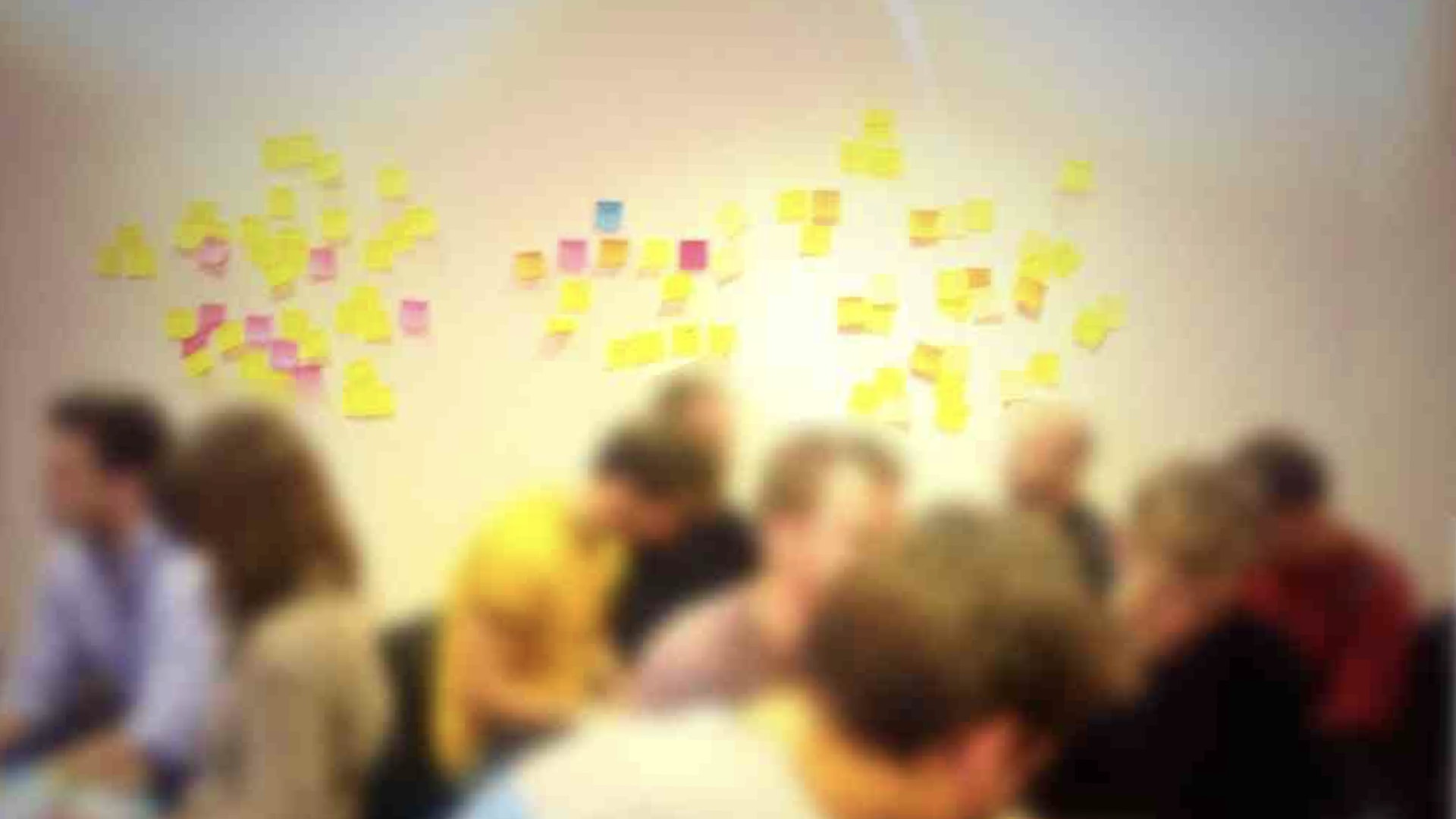 A photo of a group of people in front of a wall with lots of post-it notes on. The people have been blurred out.